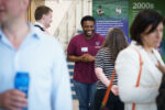 Guests talking and smiling in a bright open space while standing in front of information banners in the foyer of the NIAB building in Cambridge, UK.