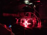 A dark lab space with tubes coming out of a bench below a machine and illuminated with a red light